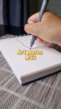 a person writing on top of a book with a pen in their hand and the word art worm written below it