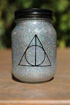 a harry potter mason jar with glitter on the lid and a hogwarts symbol painted on it