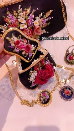 a hand holding a black purse with flowers on it and several other necklaces attached to it