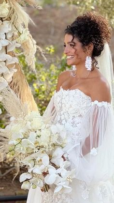 a woman in a wedding dress holding a bouquet of flowers and smiling at the camera