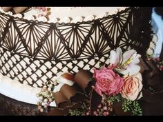 a close up of a cake with flowers on the top and chocolate ribbons around it