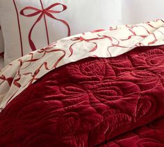 a bed with red and white comforters, pillows and bows