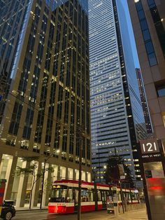 a red trolley is going down the street in front of some tall buildings at night