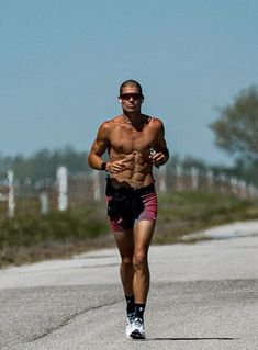 a shirtless man running down the road with no shirt on and sunglasses on his head