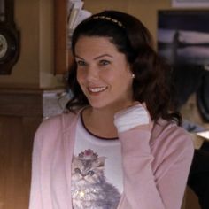 a woman wearing a pink cardigan with a cat on it's chest smiling