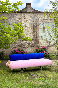 a pink and blue couch sitting on top of a lush green field next to a stone wall