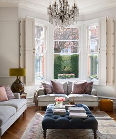 a living room filled with furniture and a chandelier hanging from the ceiling over a window