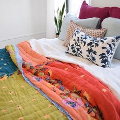 an unmade bed with colorful pillows and blankets on it's headboard, in front of a window