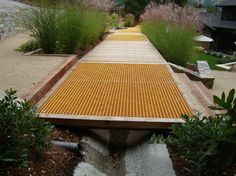 the walkway is made out of concrete and has yellow grates on it, along with plants