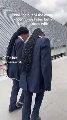 two people with long black hair standing in front of a building and looking at the sky