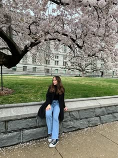 a woman sitting on a stone wall next to a tree with pink flowers in bloom