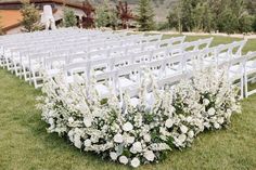 a row of white chairs sitting on top of a lush green field covered in flowers