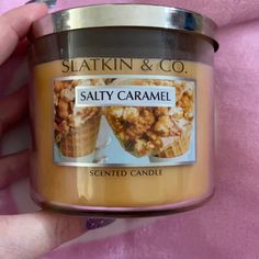 a hand holding a jar of salted caramel flavored candle on a pink blanket