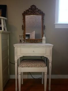 a white vanity table with a mirror and stool in front of it on a hard wood floor