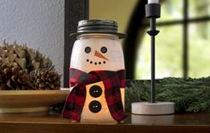 a snowman jar sitting on top of a table next to pine cones and candles