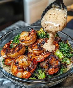 shrimp and broccoli with sauce being drizzled over them in a glass bowl