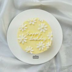 a white plate topped with a yellow and white cake covered in frosted daisies