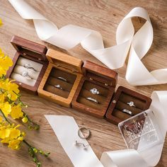 three wooden boxes with wedding rings in them next to some flowers and white satin ribbons