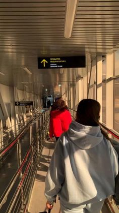 two people walking down an escalator with luggage in their hands and one person wearing a red jacket