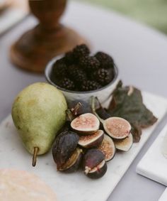 figs and other fruits are on a table next to a bowl of blackberries