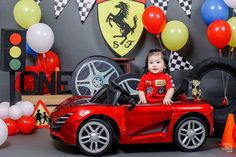 a baby boy sitting in a red sports car surrounded by balloons and streamers,