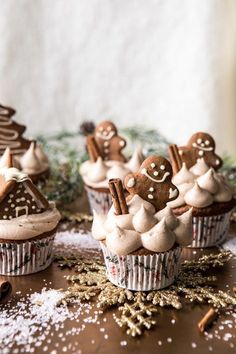 some cupcakes with frosting and gingerbread decorations on them are sitting on a table