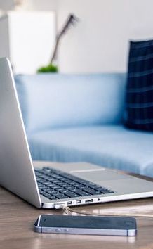 an open laptop computer sitting on top of a wooden table next to a smart phone