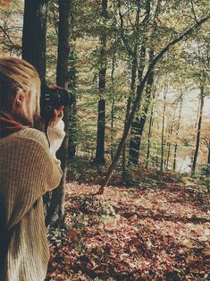 a woman standing in the woods holding a camera up to her face and taking pictures