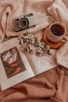 an open book, camera and cup of coffee on a bed