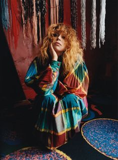 a woman sitting on the floor with her hands to her face, wearing a multicolored dress