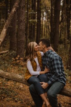 a man and woman sitting on a log in the woods kissing while they are surrounded by trees