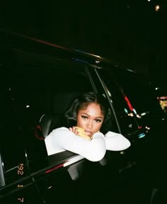 a woman sitting in the passenger seat of a car at night with her arms folded out