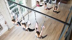 several women doing aerial exercises in a room with wood flooring and large windows on the wall