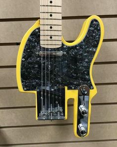 a yellow and black guitar hanging on the side of a building with it's neck missing