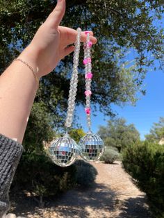 a hand holding two disco balls in front of a tree and dirt path with trees on both sides