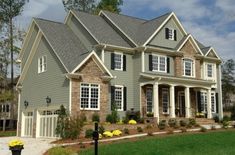 a large gray house with lots of windows and landscaping around the front door is shown