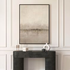 a black console table with two candles and a painting on the wall above it in a white room