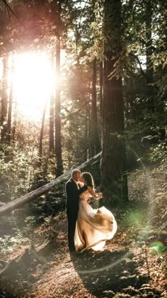 a bride and groom walking through the woods