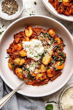 two bowls filled with pasta and sauce on top of a white tablecloth next to other dishes