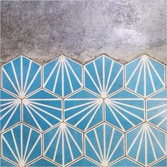 a blue and white tiled wall with geometric designs on the bottom, in front of a concrete floor