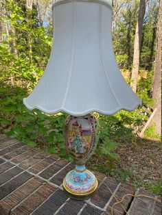 a lamp that is on top of a brick floor in front of some trees and bushes