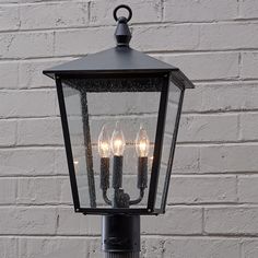 an old fashioned street light with three lights on it's side against a white brick wall