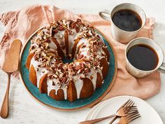 a bundt cake with white icing and pecans on a plate next to two cups of coffee