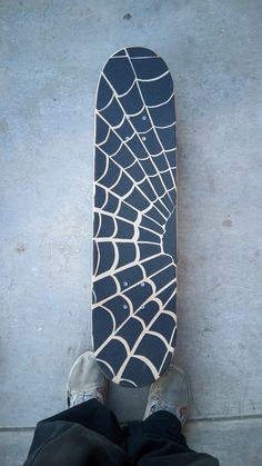 a person standing next to a skateboard with spider web design on the bottom part