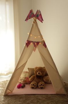 a teddy bear sitting in front of a teepee tent with lights on the top