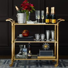 a gold bar cart filled with bottles and glasses on top of a carpeted floor