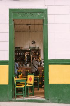 two people sitting at a table in front of a store with green and yellow chairs