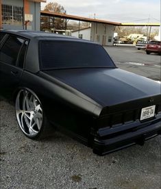 a black station wagon with chrome rims parked in front of a parking lot next to a building