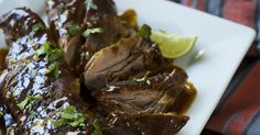 a white plate topped with meat covered in sauce and garnished with cilantro