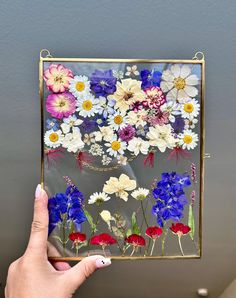 a hand holding up a glass frame with flowers on it and the bottom half painted in red, white, and blue